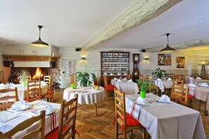 A restaurant with wooden beams, a fireplace, and multiple tables set for dining. - Logis Hotel Du Fronton-agian (Itxassou)