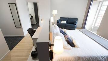 Quarto de hotel com cama, escrivaninha, cadeira, sofá, luminária e espelho.