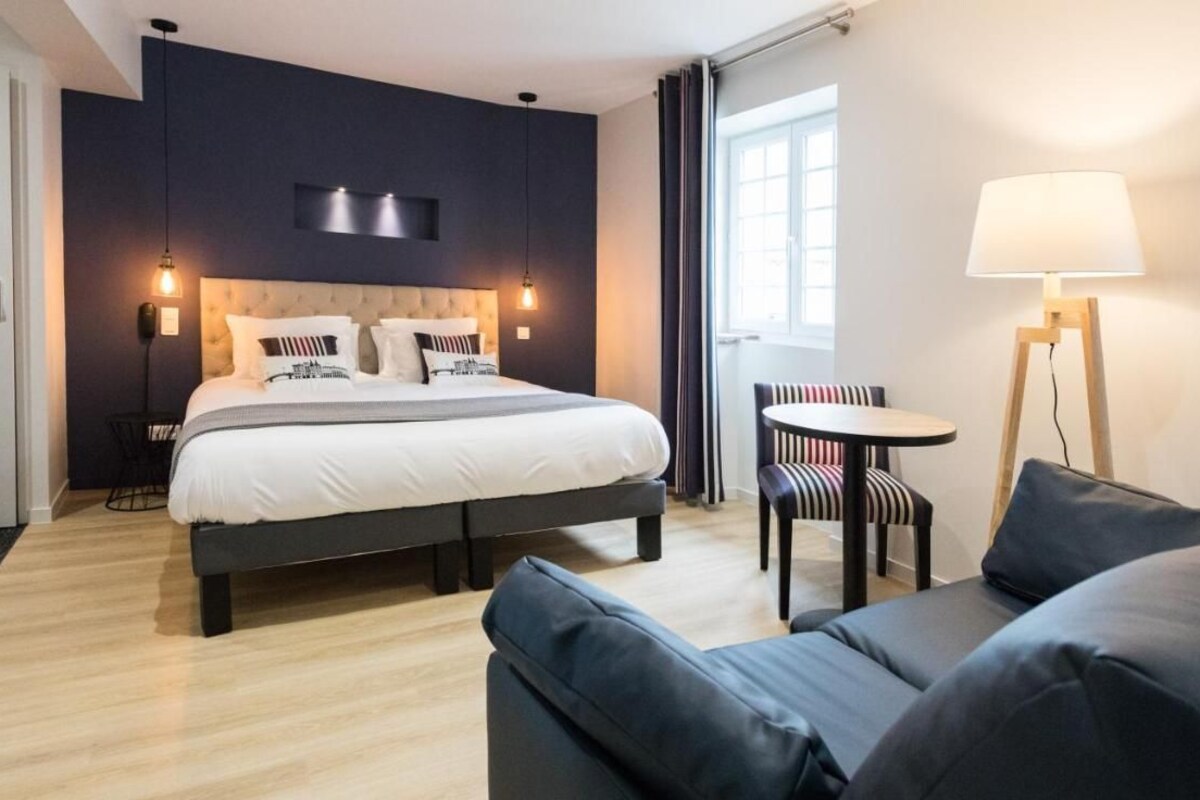 A modern hotel room with a large bed, a small round table, a sofa, and a floor lamp.
