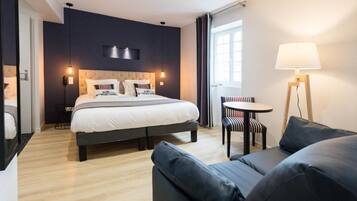 Una habitación de hotel moderna con una cama grande, una mesita redonda pequeña, un sofá y una lámpara de pie.