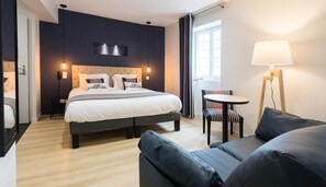 A modern hotel room with a large bed, a small round table, a sofa, and a floor lamp. - Logis Hotel Du Fronton-agian (Itxassou)