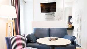 A modern living room with a sofa, a round table, a television, and a lamp. - Logis Hotel Du Fronton-agian (Itxassou)