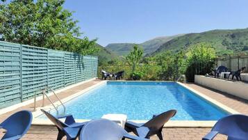 Una piscina rectangular con escalera metálica, rodeada de sillas de descanso y una cerca verde.