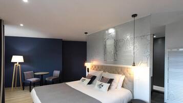 Una habitación de hotel moderna con una cama grande, una obra de arte colgada en la pared, una pequeña mesa redonda, dos sillas y una lámpara.