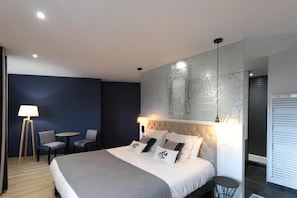 A modern hotel room with a large bed, a wall-mounted artwork, a small round table, two chairs, and a lamp. - Logis Hotel Du Fronton-agian (Itxassou)