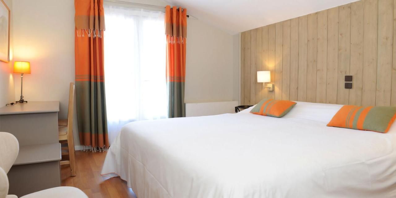 A hotel room with a large bed, a desk, a chair, and a wooden wall paneling.