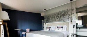 A modern hotel room with a large bed, a chair, a desk, and a wall mural. - Logis Hotel Du Fronton-agian (Itxassou)