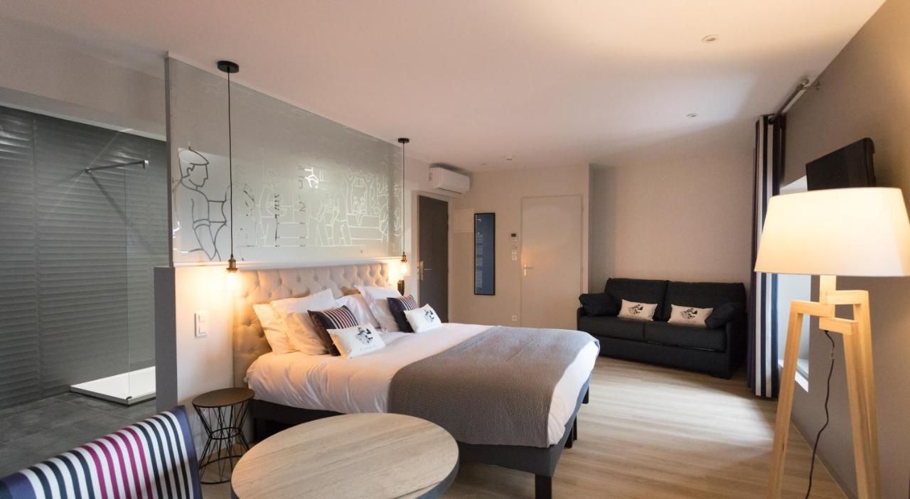 A modern hotel room with a large bed, a sofa, a small round table, and a standing lamp.