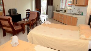 Ein Hotelzimmer mit zwei Betten, einem Esstisch, einem Fernseher, einem Kühlschrank und einer Küchenzeile.