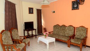 Ein Wohnzimmer mit einer Couch, zwei Sesseln, einem Fernseher und einem Tisch mit Blumenvase.
