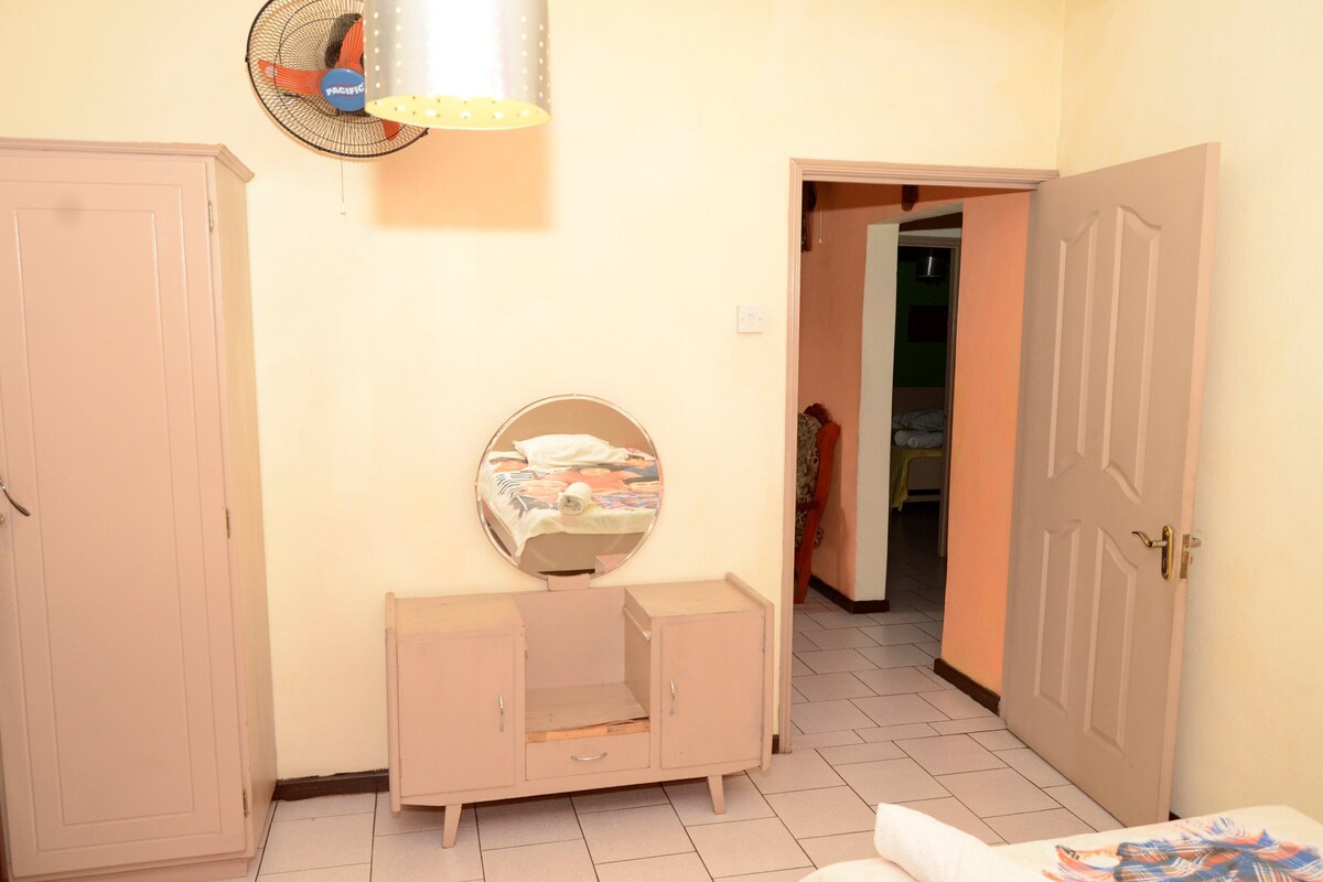 Quarto com cama, guarda-roupa, espelho e ventoinha.