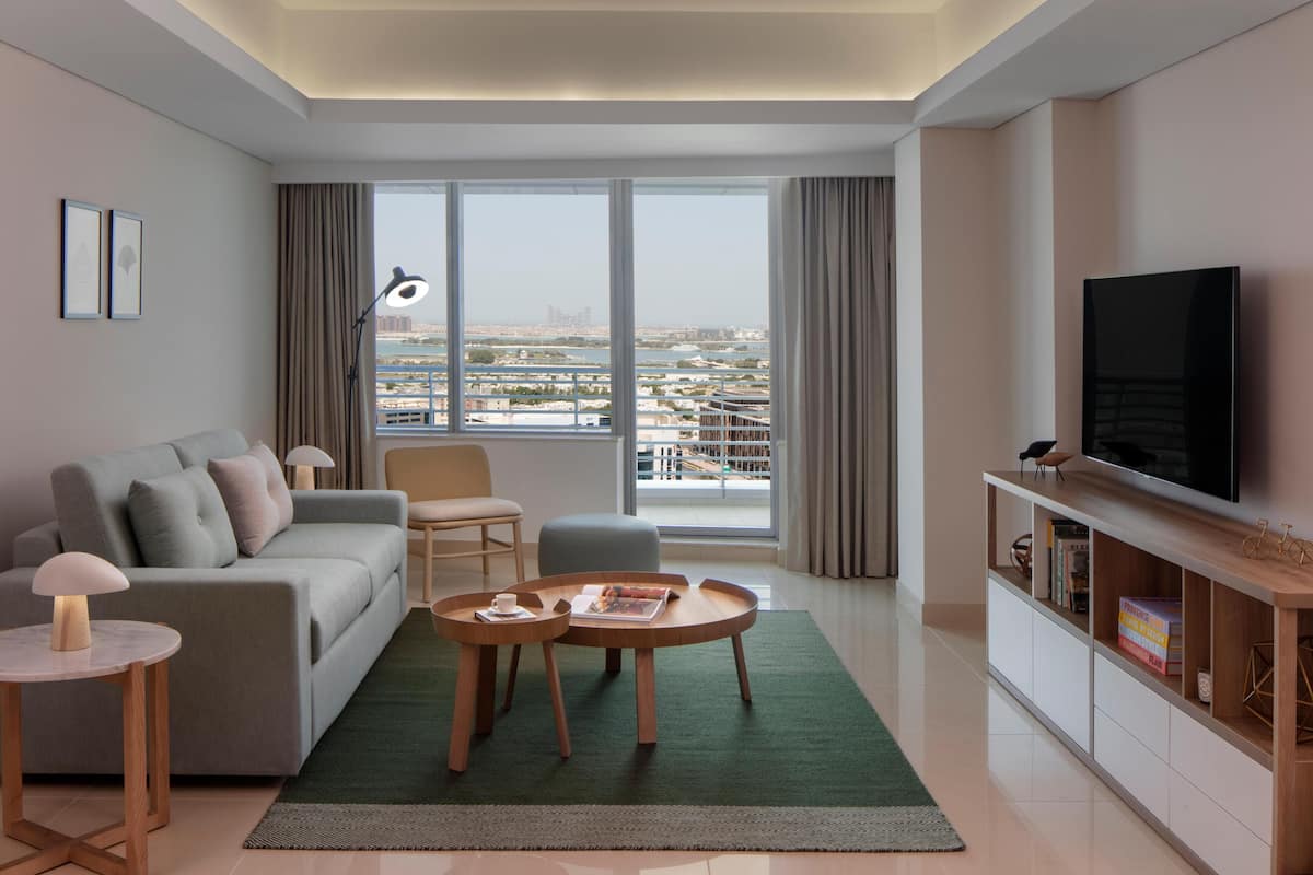 Ein modernes Wohnzimmer mit einer Couch, zwei Tischen, einem Fernseher und Blick auf eine Skyline durch große Fenster.