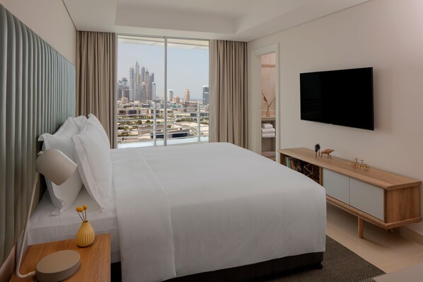 A hotel room with a large bed, a TV mounted on the wall, a wooden console table, and a view of a cityscape. - Staybridge Suites Dubai Internet City (DUBAI)