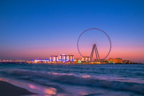A waterfront view with a large Ferris wheel and illuminated buildings. - Staybridge Suites Dubai Internet City (DUBAI)