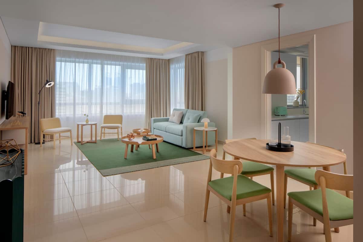 Ein modernes Hotelzimmer mit Wohnbereich, Esstisch und Blick auf die Stadt.