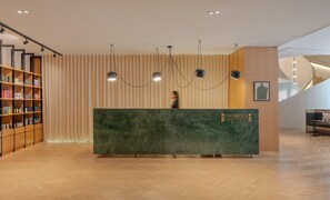 A reception desk with a marble top, a wooden bookshelf with various items, and a modern light fixture.