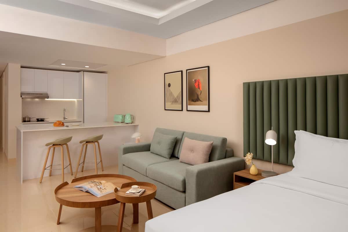 Ein modernes Hotelzimmer mit Bett, einer Couch, einem Esstisch und einer Küchenzeile.