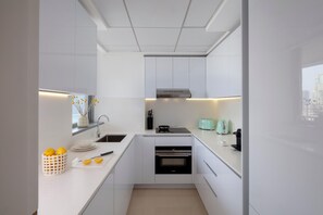 A modern kitchen with white cabinetry, a built-in oven, a coffee maker, and a window with a city view. - Staybridge Suites Dubai Internet City (DUBAI)