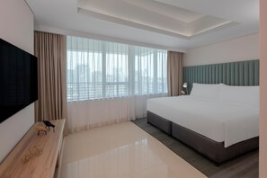 Ein modernes Hotelzimmer mit einem großen Bett, einem Flachbildfernseher, einer Holzbank und Blick auf die Stadt.