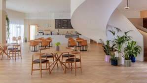 A spacious indoor area with wooden flooring, tables, chairs, and potted plants.