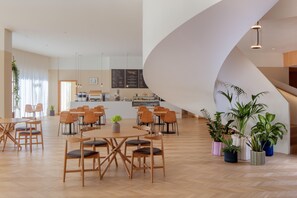 A spacious indoor area with wooden flooring, tables, chairs, and potted plants.