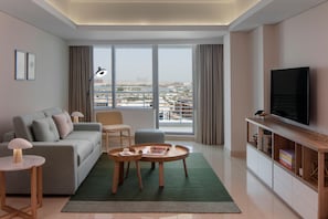 A modern living room with a sofa, two round tables, a TV, and a view of a cityscape through large windows. - Staybridge Suites Dubai Internet City (DUBAI)
