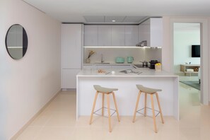 A modern kitchen with white cabinetry, a central island with stools, and a flat-screen TV mounted on the wall. - Staybridge Suites Dubai Internet City (DUBAI)