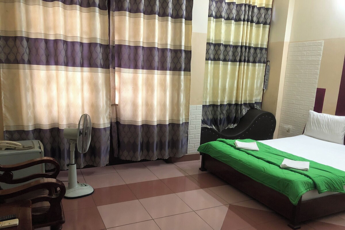 Une chambre d’hôtel avec un lit, une chaise, un bureau, un ventilateur et des rideaux.