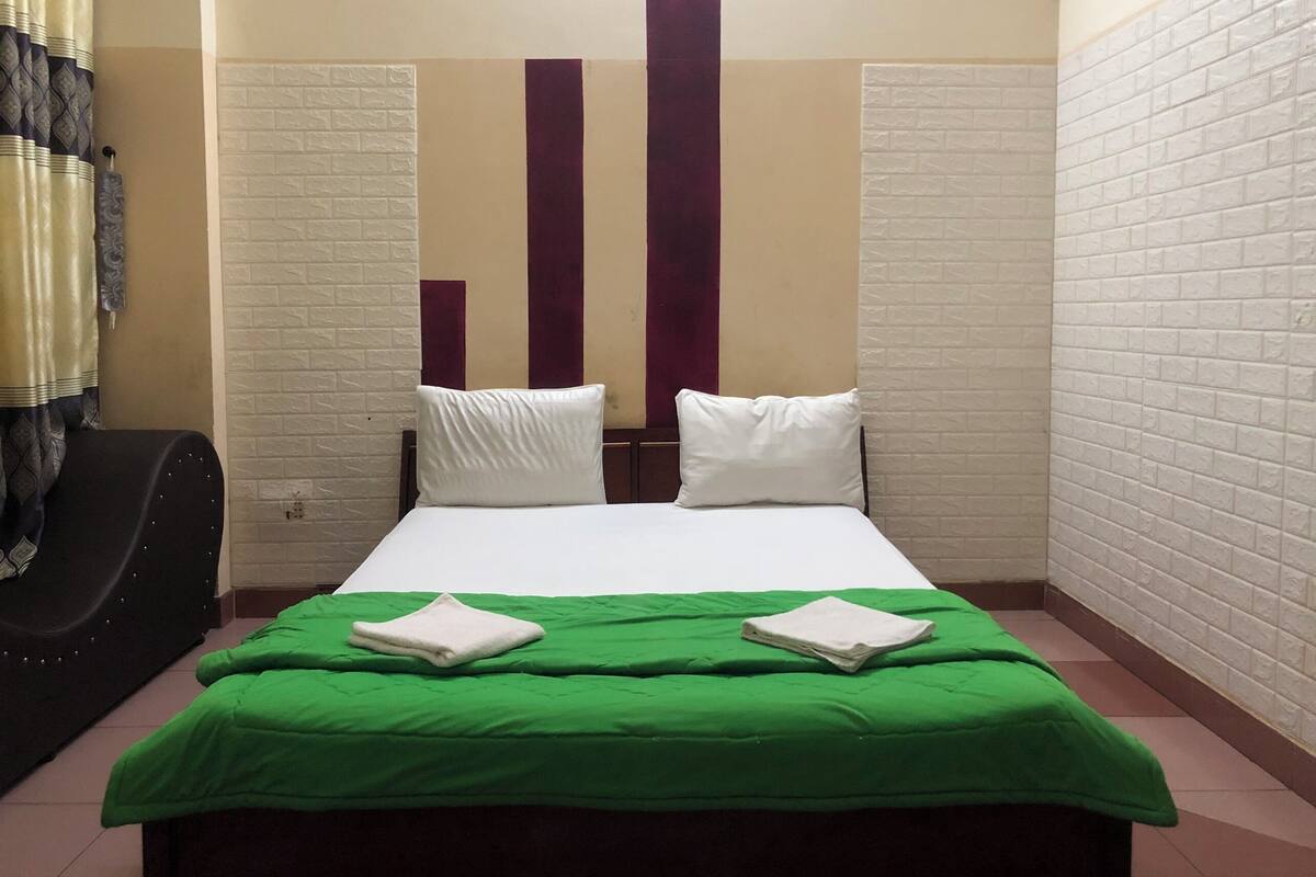 Ein Hotelzimmer mit Bett, grüner Bettdecke, weißen Kissen und einem schwarzen Stuhl.