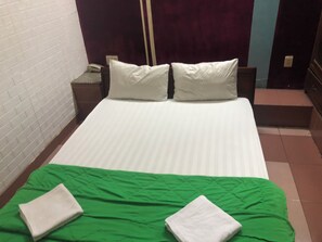 Une chambre d’hôtel avec un lit, deux oreillers, une couvre-lit verte et deux serviettes pliées.