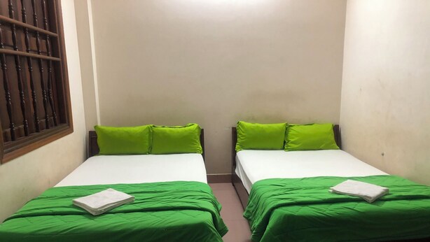 Twee eenpersoonsbedden met groene beddengoed en kussens, een raam met tralies en een witte muur.