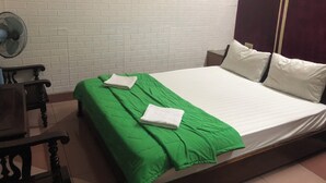 Een kamer met een bed, een ventilator, een houten stoel en een witte bakstenen muur.