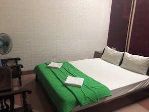 Ein Zimmer mit einem Bett, einem Ventilator, einem Holzbett und einer weißen Ziegelwand.
