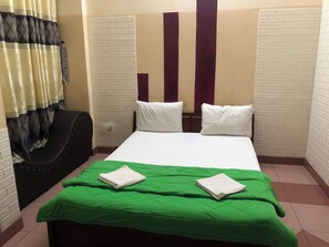 Ein Hotelzimmer mit Bett, Kissen, einer grünen Tagesdecke, einem schwarzen Sessel und einem Vorhang.