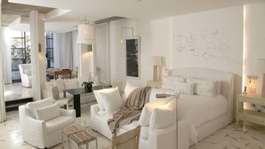 A modern hotel room with a large bed, white furniture, a dining area, and a view through the window. - Lotel at Doce18 Concept House (San Miguel de Allende)