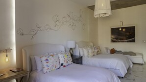 A hotel room with two beds, a nightstand, a lamp, a wall art of branches, and a cityscape painting. - Lotel at Doce18 Concept House (San Miguel de Allende)