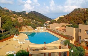 A swimming pool with lounge chairs, surrounded by buildings and hills. - Amazing apartment in Costa Paradiso with swimming pool (Costa Paradiso)