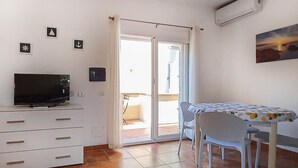 Een kamer met een televisie, een tafel met stoelen, een schuifdeur naar een balkon, en een schilderij aan de muur.