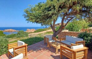 An outdoor seating area with a table and chairs, a tree, and a view of the sea. - Amazing apartment in Costa Paradiso with swimming pool (Costa Paradiso)