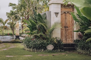 A garden with a wooden door, lush greenery, and a stone sign. - Aswanaya Villas & Suite (Ubud)