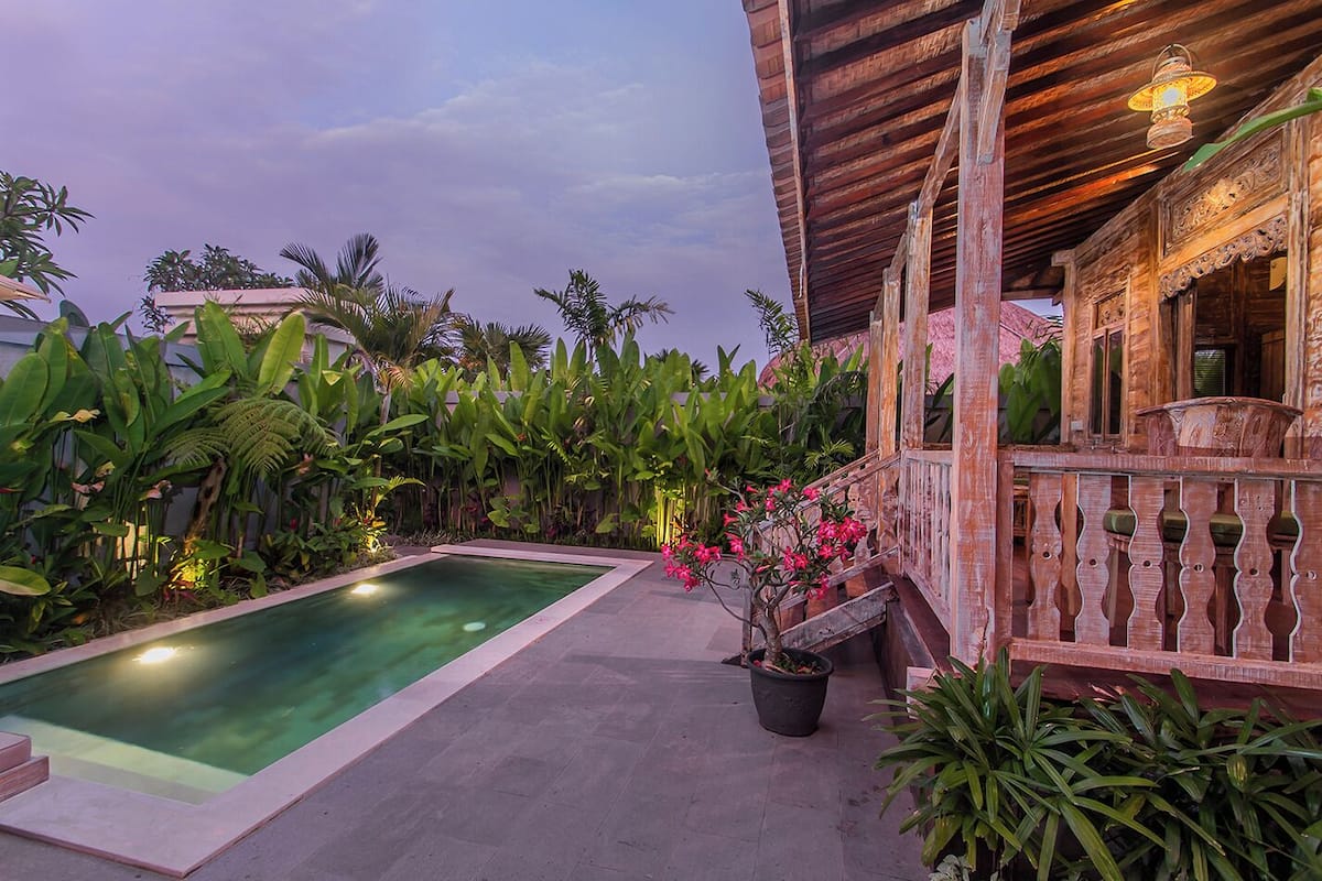 Una piscina con cubierta de madera, rodeada de exuberante vegetación tropical y una estructura de madera con barandilla.