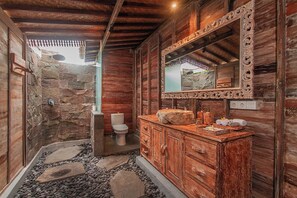 A rustic bathroom with a stone wall, wooden vanity, and a large mirror.