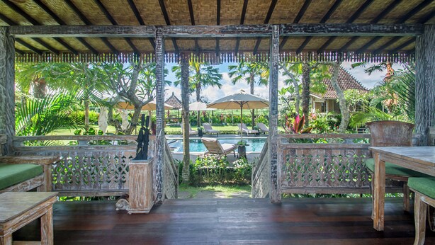 A covered outdoor area with wooden furniture, a pool, and lush greenery. - Aswanaya Villas & Suite (Ubud)