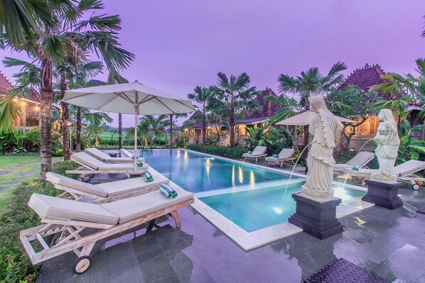 A pool area with lounge chairs, umbrellas, and statues.