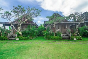 A traditional wooden structure with a staircase leading to a porch, surrounded by lush greenery and a clear sky.