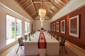 A conference room with a long table, chairs, a chandelier, framed artwork, and large windows.