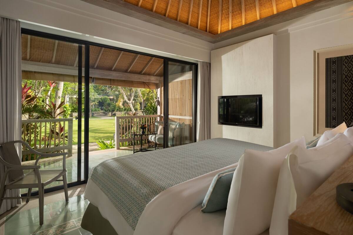 Un dormitorio con una cama grande, televisión y balcón con mobiliario exterior.