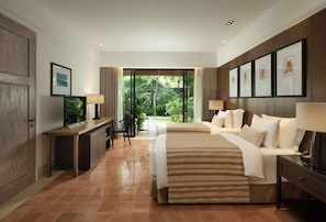 A hotel room with a bed, desk, TV, and large windows with a view of greenery. - Sudamala Resort, Komodo, Labuan Bajo (LABUAN BAJO)