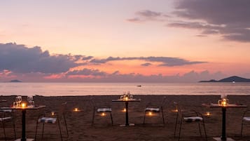 Ein Essbereich am Strand mit Tischen und Stühlen mit Blick auf das Meer.