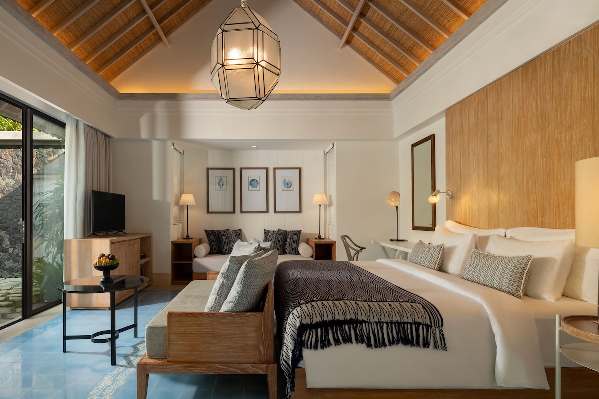 A modern bedroom with a large bed, a TV, and a dining area with a table and chairs.